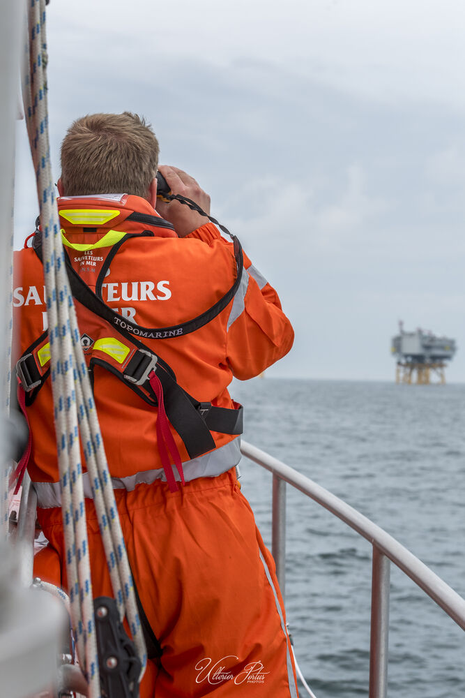 Sauveteur embarqué, sur un bateau, qui regarde l'horizon avec des jumelles